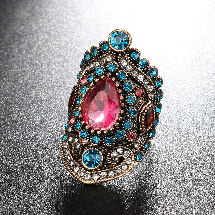 Decorative brooch with a pink teardrop gem and blue accents on a reflective surface