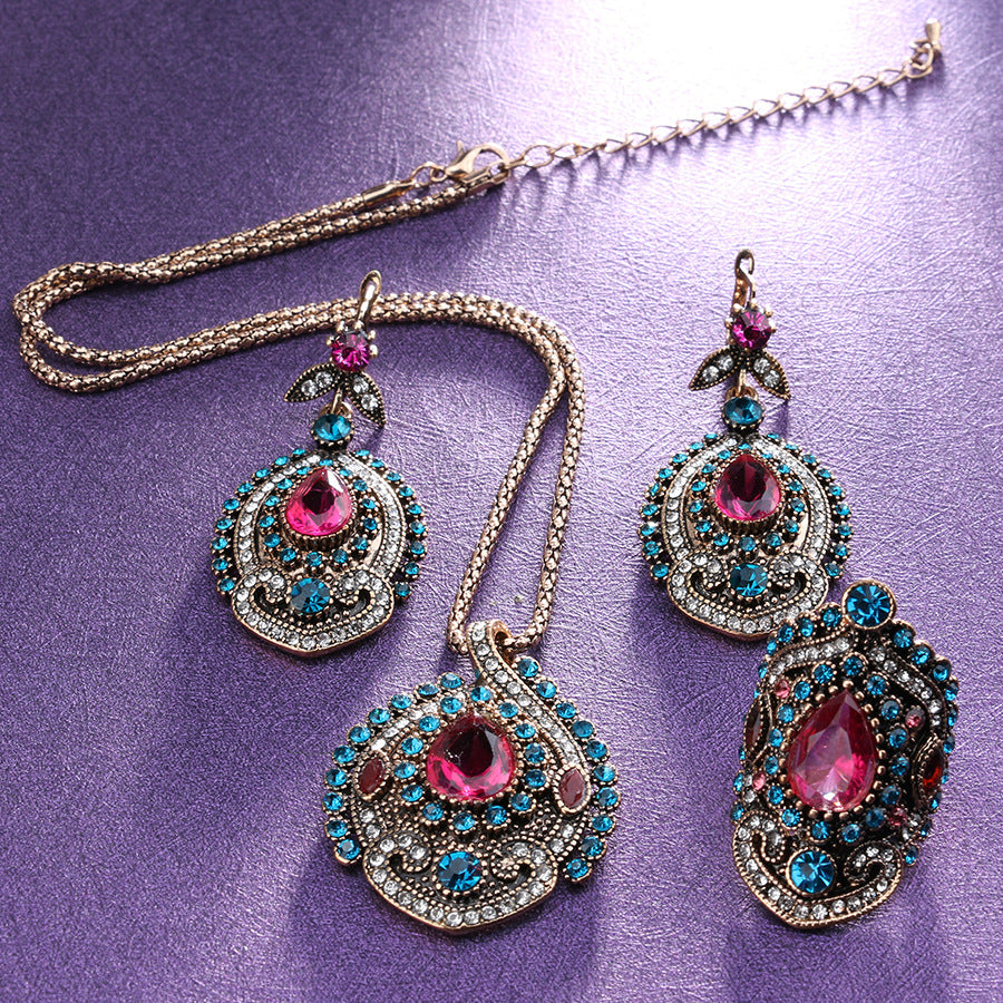 Ornate necklace and earrings with pink and blue gemstones on a purple background